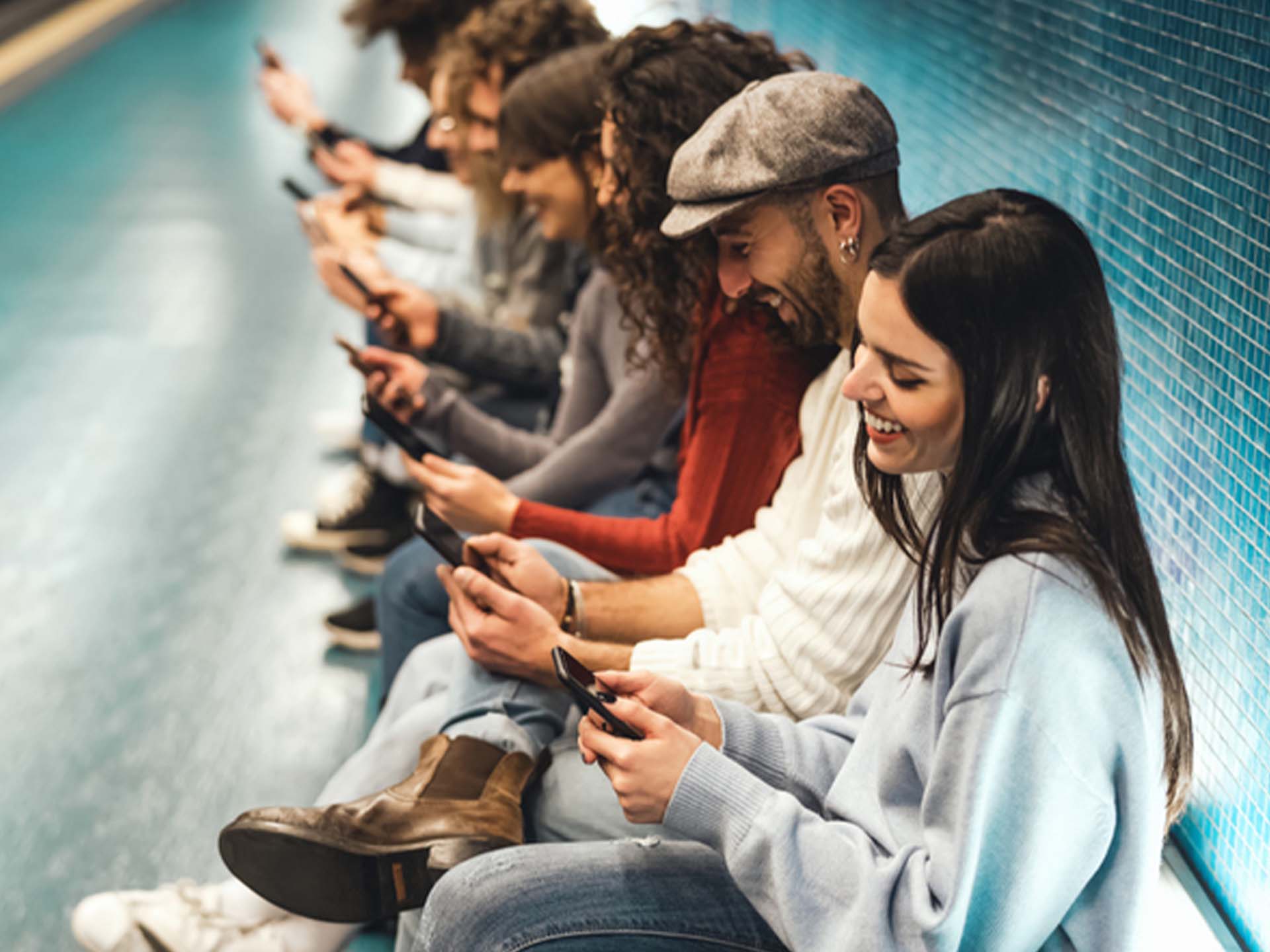 Gruppe sitzt auf dem U-Bahnsteig und spielt mit den Handys. Spielen.