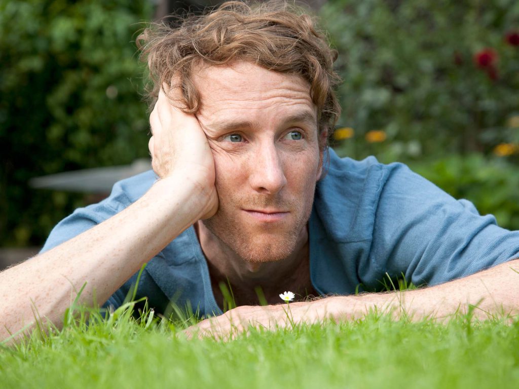 Ein Mann, der entspannt auf dem Rasen liegt und über seine Männergesundheit nachdenkt.