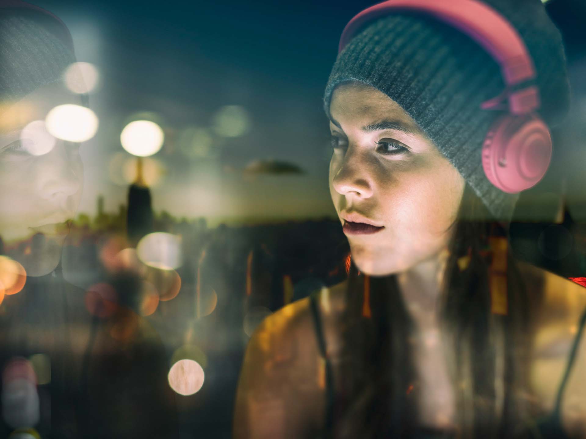 Junge Frau mit Kopfhörer auf schaut auf die blendenden Lichter der Stadt. Migräne Kolumne