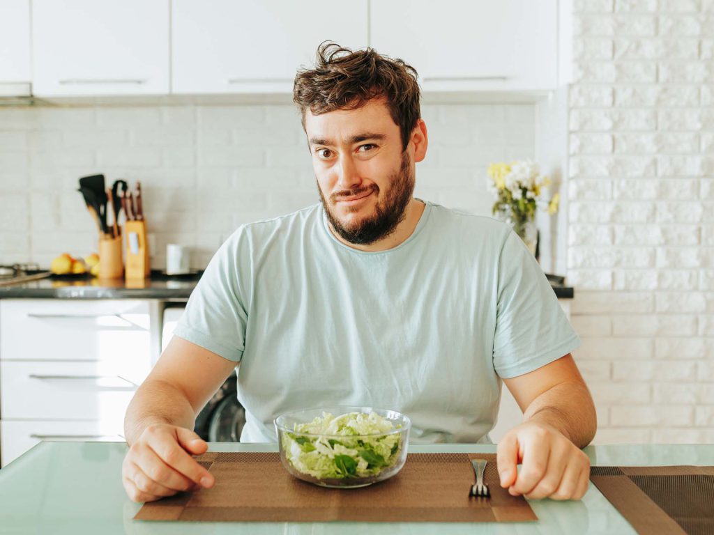 Mann, mitleren Alters, schaut skeptisch auf eine Schüssel Salat. Thema Männergesundheit, gesunde Ernährung
