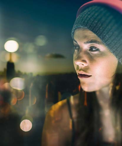 Junge Frau mit Kopfhörer auf schaut auf die blendenden Lichter der Stadt. Migräne Kolumne