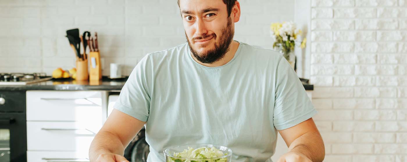 Mann, mitleren Alters, schaut skeptisch auf eine Schüssel Salat. Thema Männergesundheit, gesunde Ernährung